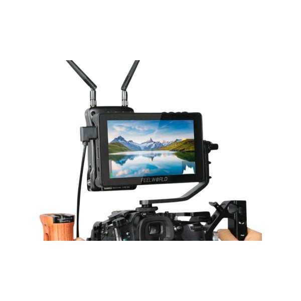Feelworld F5 PRO V4 6" -monitori on asennettu kameralaitteeseen, ja se näyttää maiseman, jossa on vuoria, järvi ja sininen taivas; kaksi antennia on kiinnitetty monitoriin.
