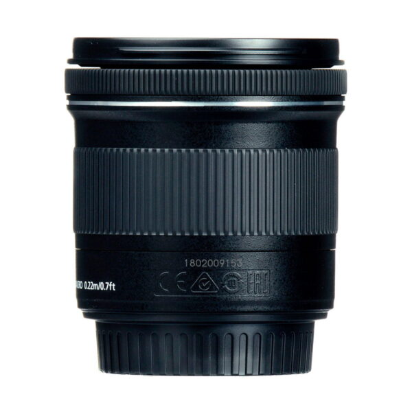 Lähikuva Canon EF-S 10-18mm f/4.5-5.6 IS STM -objektiivista näyttää sen mustat, kuvioidut tarkennusrenkaat ja zoomausrenkaat, joissa on valkoisia merkintöjä ja symboleja lähellä pohjaa, kaikki valkoista taustaa vasten.