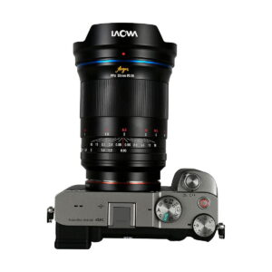Top view of a silver digital camera with control dials, buttons and a textured right-hand grip on which a large Laowa Argus 35mm f/0.95 FF - Sony-E lens is mounted.