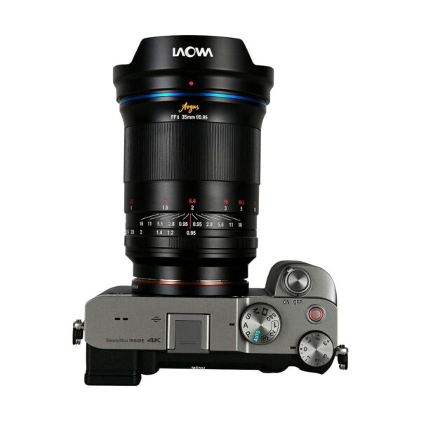 Top view of a silver digital camera with control dials, buttons and a textured right-hand grip on which a large Laowa Argus 35mm f/0.95 FF - Sony-E lens is mounted.