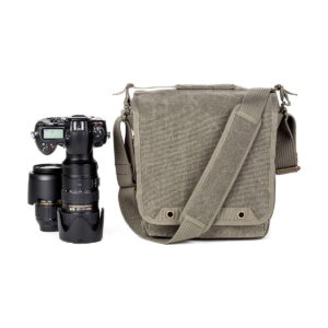 DSLR-kamera, jossa on pitkä zoom-objektiivi ja ylimääräinen objektiivi, on sijoitettu Think Tank Retrospective 20 V2.0 - Pinestone -lähettiläsmallinen kameralaukku, jossa on olkahihna, viereen valkoista taustaa vasten.