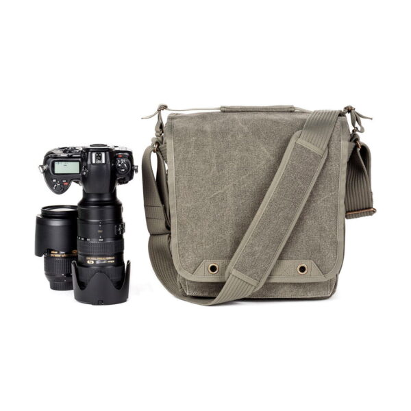 DSLR-kamera, jossa on pitkä zoom-objektiivi ja ylimääräinen objektiivi, on sijoitettu Think Tank Retrospective 20 V2.0 - Pinestone -lähettiläsmallinen kameralaukku, jossa on olkahihna, viereen valkoista taustaa vasten.