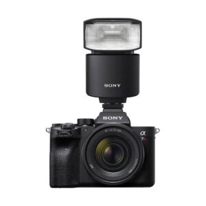 Musta Sony-digitaalikamera, jossa on zoom-objektiivi ja suuri käsisalama, Sony HVL-F46RM, asennettuna päälle, kuvattuna valkoista taustaa vasten.