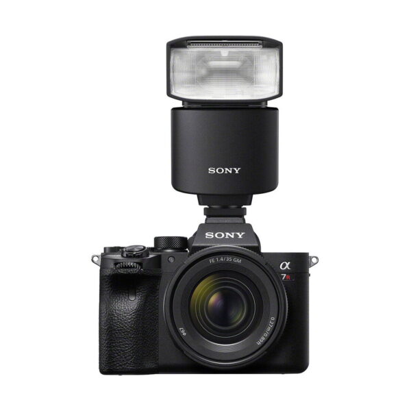 Musta Sony-digitaalikamera, jossa on zoom-objektiivi ja suuri käsisalama, Sony HVL-F46RM, asennettuna päälle, kuvattuna valkoista taustaa vasten.