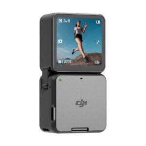 The grey DJI Action 2 Dual-Screen Combo action camera has a folding screen and shows footage of a woman running across rocky terrain under a blue sky, combining compact size with a simple, modern design.