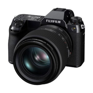 Musta Fujifilm GFX 100S -järjestelmäkamera, jossa on suuri irrotettava objektiivi, useita ohjauspainikkeita ja valintakiekkoja, näkyy vinossa valkoista taustaa vasten.