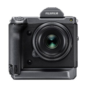 Fujifilm GFX 100 -digitaalikameran etukuva, jossa on suuri objektiivi, kuvioitu kahva ja sisäänrakennettu pystysuora akkukahva, valkoista taustaa vasten.