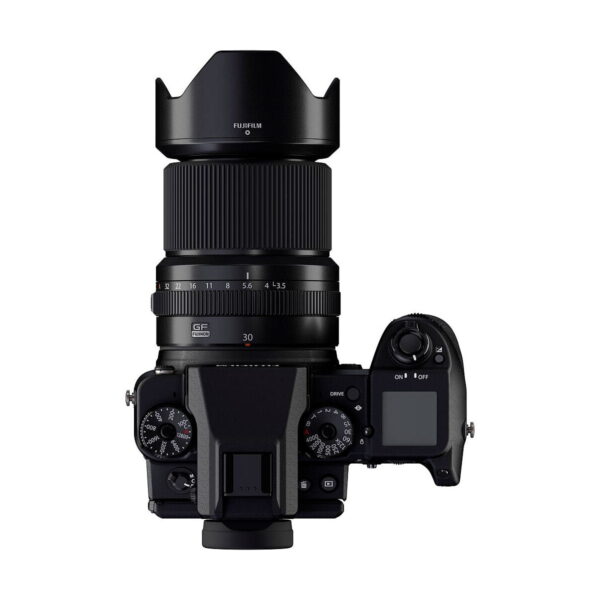 Ylhäältä katsottuna musta Fujifilm-kamera, jossa on Fujinon GF 30mm f/3.5 R WR -objektiivi, jossa on suuri objektiivi ja huppu, näkyvät säätöpyörät, painikkeet ja LCD-näyttö oikealla puolella.