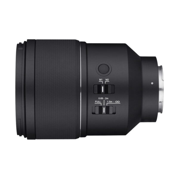 Samyang_AF_135mm_F_1_8_Sony-FE_003 Samyang AF 135mm F/1.8 - Sony FE -objektiivin sivukuva mustana, jossa on ohjauskytkimet, painikkeet, kuvioitu tarkennusrengas ja metallinen objektiivin kiinnike oikealla, valkoista taustaa vasten.