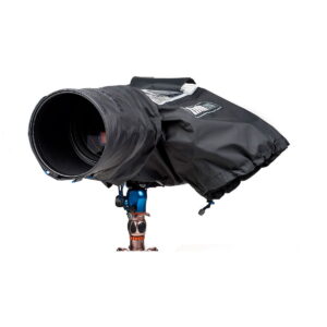 Think Tank Hydrophobia DM 300-600 V3 -sadesuoja suojaa suurta kameraa, jossa on pitkä objektiivi ja joka on kiinnitetty siniseen ja kupariseen jalustaan valkoista taustaa vasten.
