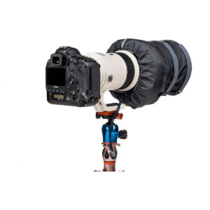 Think Tank Hydrophobia DM 300-600 V3 musta sadesuoja peittää ammattikäyttöön tarkoitetun DSLR-kameran, jossa on suuri teleobjektiivi ja joka on asennettu jalustalle, jossa on sinisiä ja kuparisia korostuksia valkoista taustaa vasten.