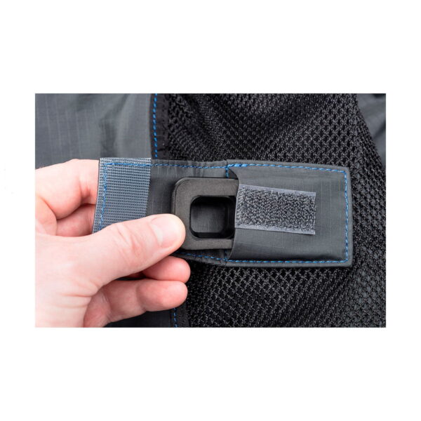 Kädessä on Think Tank Hydrophobia DM 300-600 V3, jossa näkyy sen musta kangashihna, jossa on siniset tikkaukset, tarranauha ja musta verkkomateriaali.