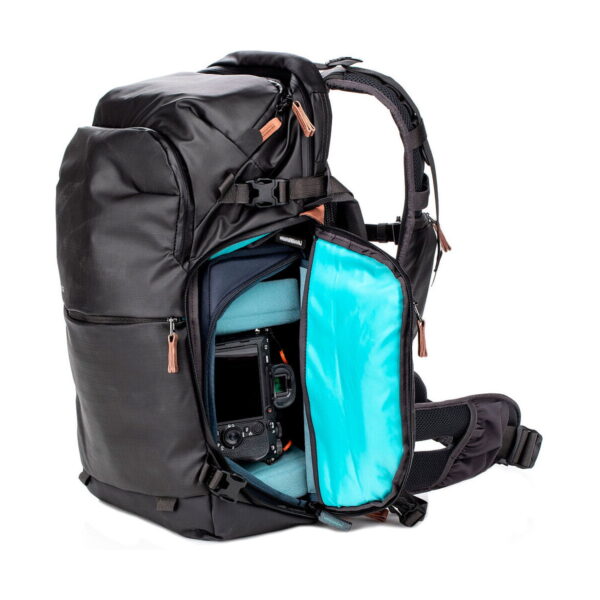 Shimoda Designs Explore v2 25 Starter Kit -kamerareppu, musta, sisältää pehmustetun sinisen sisustan, useita lokeroita kameravarusteiden järjestettyyn säilytykseen ja ruskeat vetoketjunvetimet. Osittain avattu vetoketju paljastaa kameran turvallisesti säilöttynä sisälle.