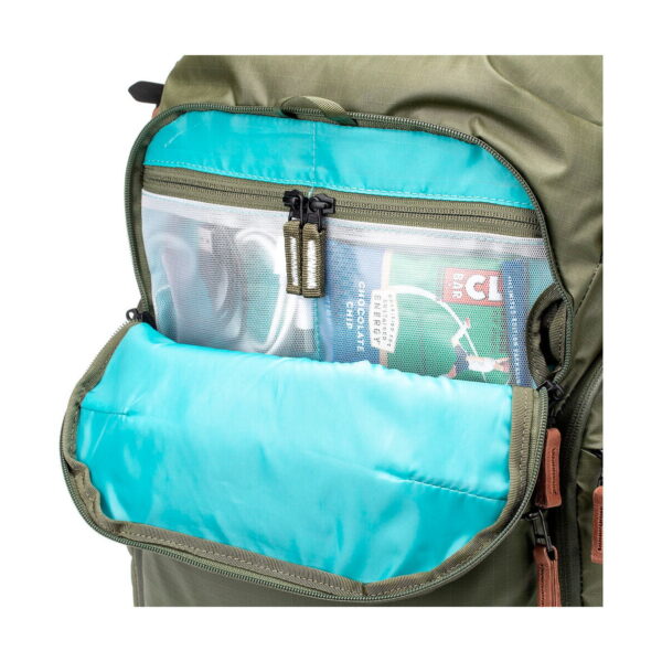 Close-up of the Shimoda Designs Explore v2 25 Starter Kit camera backpack in green, showing its open pocket with turquoise lining, zippered mesh pocket and storage space for rolled magazine and small items.