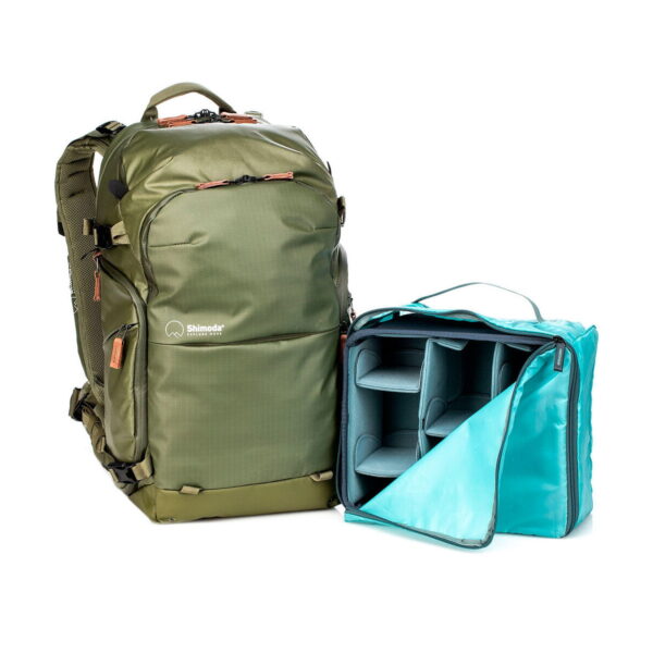 The green Shimoda Designs Explore v2 25 Starter Kit camera backpack stands next to an open, removable turquoise camera equipment insert with adjustable padded dividers for organizing your photography gear.
