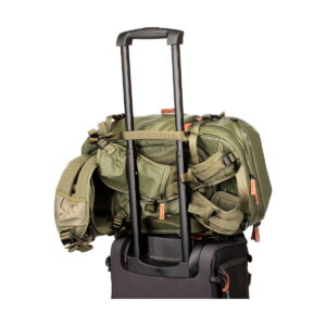 The Shimoda Designs Explore v2 25 Starter Kit camera backpack, green, is securely attached to the extended handle of a black roller bag, isolated by a white background.