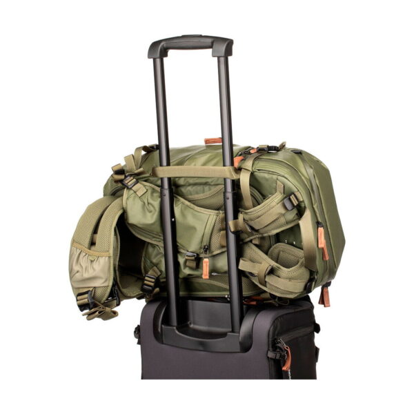 The Shimoda Designs Explore v2 25 Starter Kit camera backpack, green, is securely attached to the extended handle of a black roller bag, isolated by a white background.