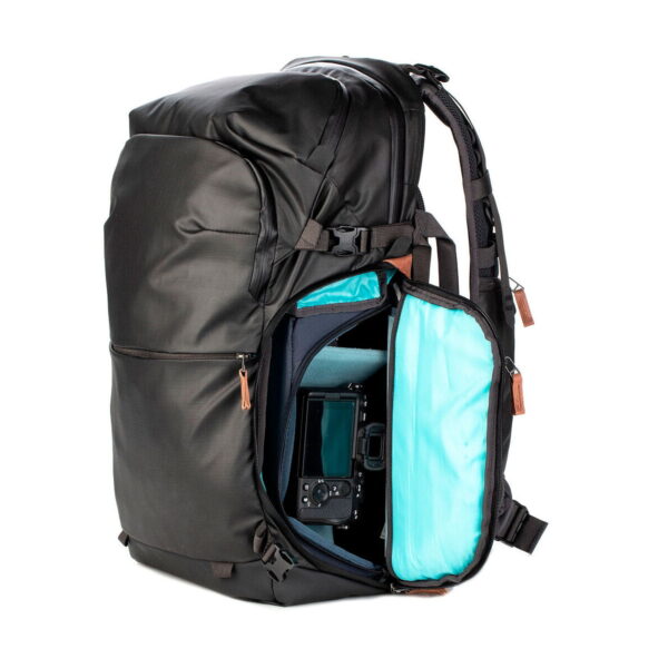 The Shimoda Designs Explore v2 30 Camera Backpack in black features a side compartment that opens with a zipper to reveal the camera and a bright blue interior with multiple pockets and brown zipper pulls.