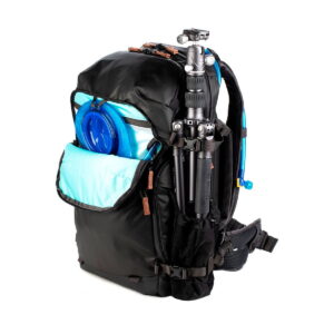 The Shimoda Designs Explore v2 30 Camera Backpack, Black features a light blue front pocket, a blue frisbee holder, a side-mounted stand and a blue hydration tube. It has multiple compartments and padded shoulder straps.