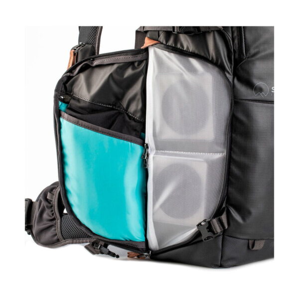 Close-up of the Shimoda Designs Explore v2 30 camera backpack, the black side pocket shows organized compartments with blue insert, a zippered mesh compartment and two cylindrical objects inside.