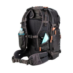 The Shimoda Designs Explore v2 30 camera backpack, black, features a white base with padded shoulder straps, multiple pockets and a hipbelt; a water bottle and smartphone are stored in the side and hipbelt pockets.