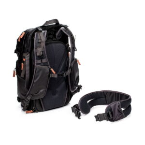 The Shimoda Designs Explore v2 30 Camera Backpack, Black is presented in an upright position with multiple compartments and brown zipper pulls next to its removable padded waist strap on a white base.