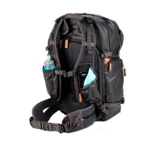 Shimoda Designs Explore v2 35 Camera Backpack, Black is a black travel backpack with multiple compartments, zippers, padded shoulder straps, hip belt and side pockets to hold a water bottle and a folded blue object, shown against a white background.