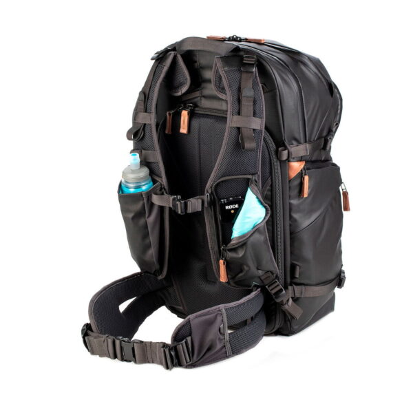 Shimoda Designs Explore v2 35 Camera Backpack, Black is a black travel backpack with multiple compartments, zippers, padded shoulder straps, hip belt and side pockets to hold a water bottle and a folded blue object, shown against a white background.