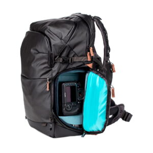 The Shimoda Designs Explore v2 35 camera backpack, black, is shown partially opened to reveal its padded camera compartment with digital camera and bright blue inner lining. Brown zipper pulls accentuate the black backpack.
