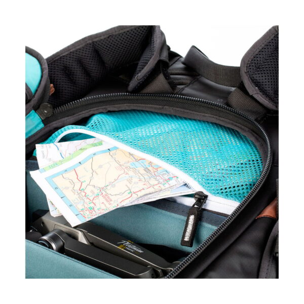 Close-up of the Shimoda Designs Explore v2 35 camera backpack, black showing the map partially hidden in the blue mesh pocket, the zipped compartment and part of the camera inside.