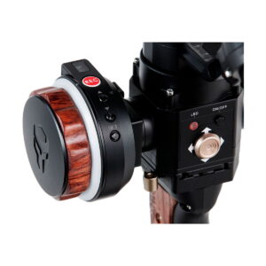 Close-up of Tilta's Nucleus-Nano Wireless Focus Control System, showing the wood-patterned selection dial, REC button, joystick, labelled buttons, LED indicator light and toggle switch for precise focusing of the camera.