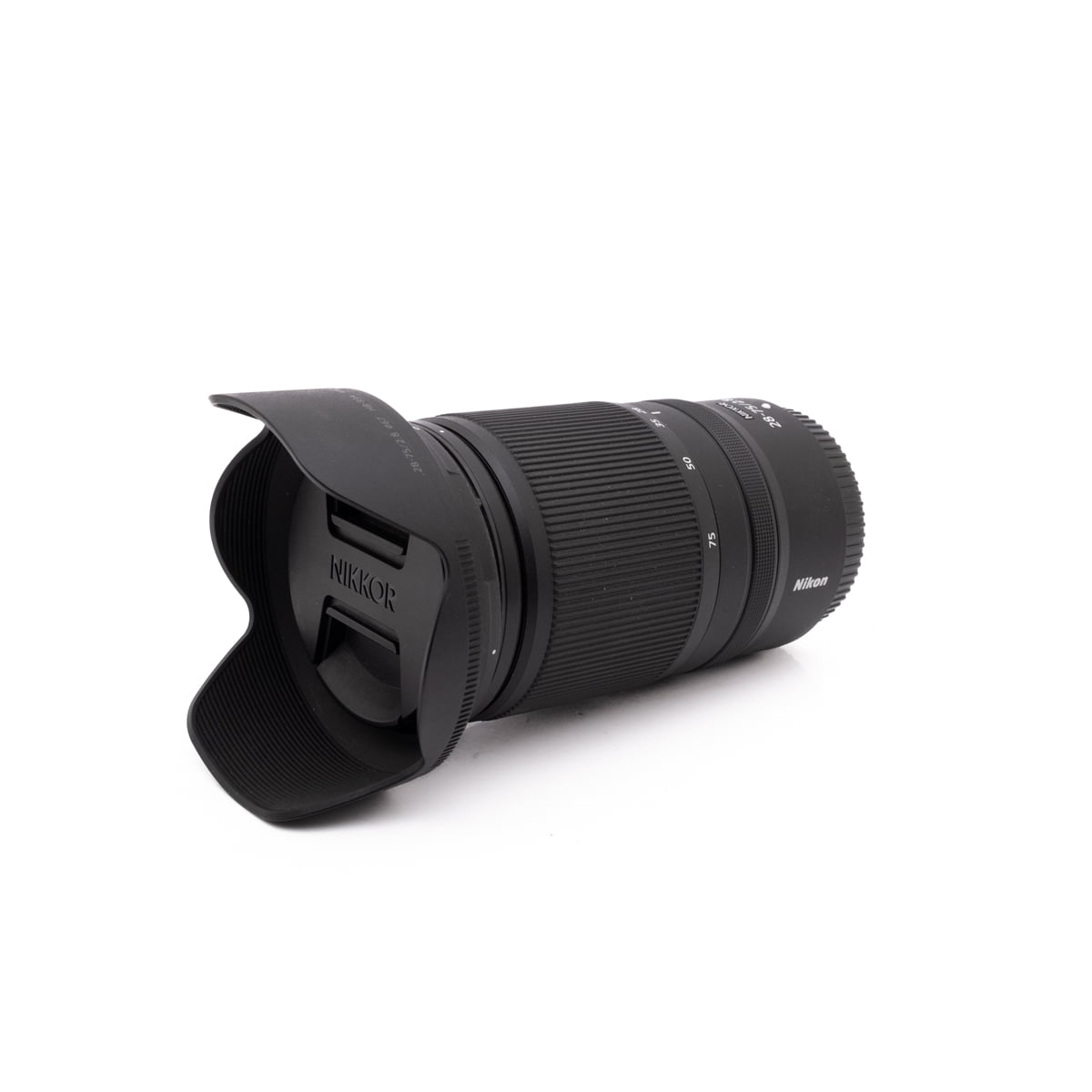 Nikkor 28-75mm f2.8-1 Sigma 30mm f/1.4 DC DN Sony E - Käytetty objektiivi, johon on kiinnitetty vastavalosuoja, lepää valkoisella pinnalla kulmassa, joka korostaa tuotemerkkiä ja kuvioitua kahvaa.