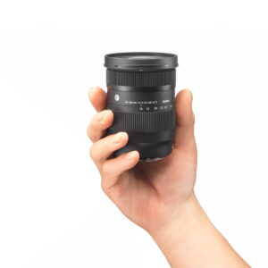 Käsi pitää Sigma 16-28mm f/2.8 DG DN Contemporary -objektiivi Sony E:lle valkoista taustaa vasten.