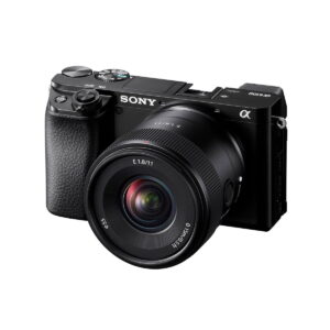 Musta Sony Alpha 6100 -peilittömäkamera, johon on kiinnitetty Sony E 11mm f/1.8 -objektiivi, vinossa valkoista taustaa vasten.