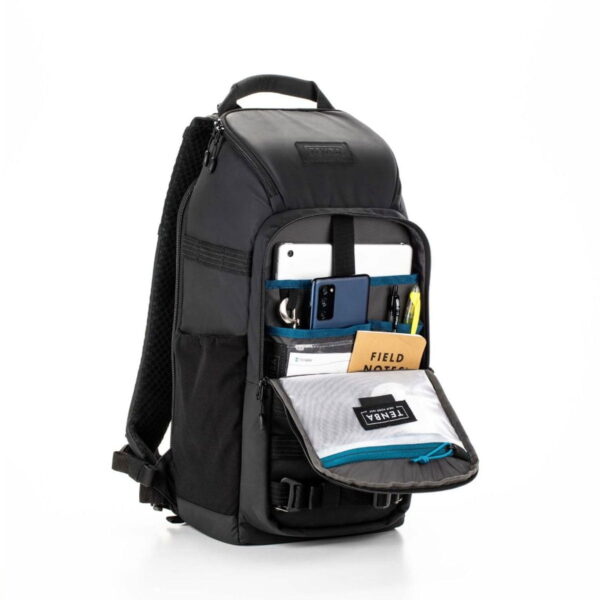Tenba Axis V2 16L Backpack -kamerareppu seisoo pystyssä etutasku auki vetoketjulla ja näyttää järjestetyt lokerot puhelimelle, tabletille, kynille, muistikirjalle ja verkkopussille, jossa on merkintä TENBA. Siinä on pehmustetut hihnat ja yläkahva.