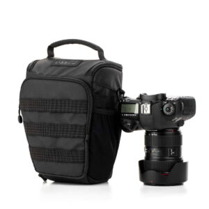Tenba Axis V2 4L Top Loader -kameralaukku, jossa on kahva, istuu ammattikäyttöön tarkoitetun DSLR-kameran vieressä, jossa on suuri objektiivi ja suojus, molemmat valkoista taustaa vasten.