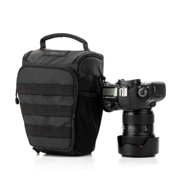 Tenba Axis V2 4L Top Loader -kameralaukku, jossa on kahva, istuu ammattikäyttöön tarkoitetun DSLR-kameran vieressä, jossa on suuri objektiivi ja suojus, molemmat valkoista taustaa vasten.