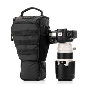 Musta DSLR-kamera, jossa on suuri valkoinen teleobjektiivi, seisoo pystyssä Tenba Axis V2 4L Top Loader -laitteen vieressä, joka on pehmustettu musta kamerakotelo, jossa on vetoketjut ja yläkahva.