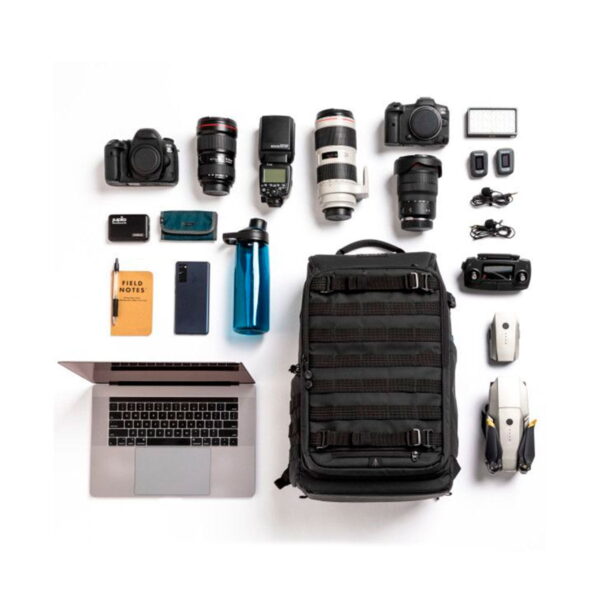 Flat lay -kuva, jossa Tenba Axis V2 24L -reppu -kamerareppu on kahden kameran, objektiivien, kannettavan tietokoneen, kannettavan tietokoneen, puhelimen, vesipullon, lennokin, hiiren, latureiden ja tarvikkeiden kanssa siististi järjestettynä valkoisella pohjalla.