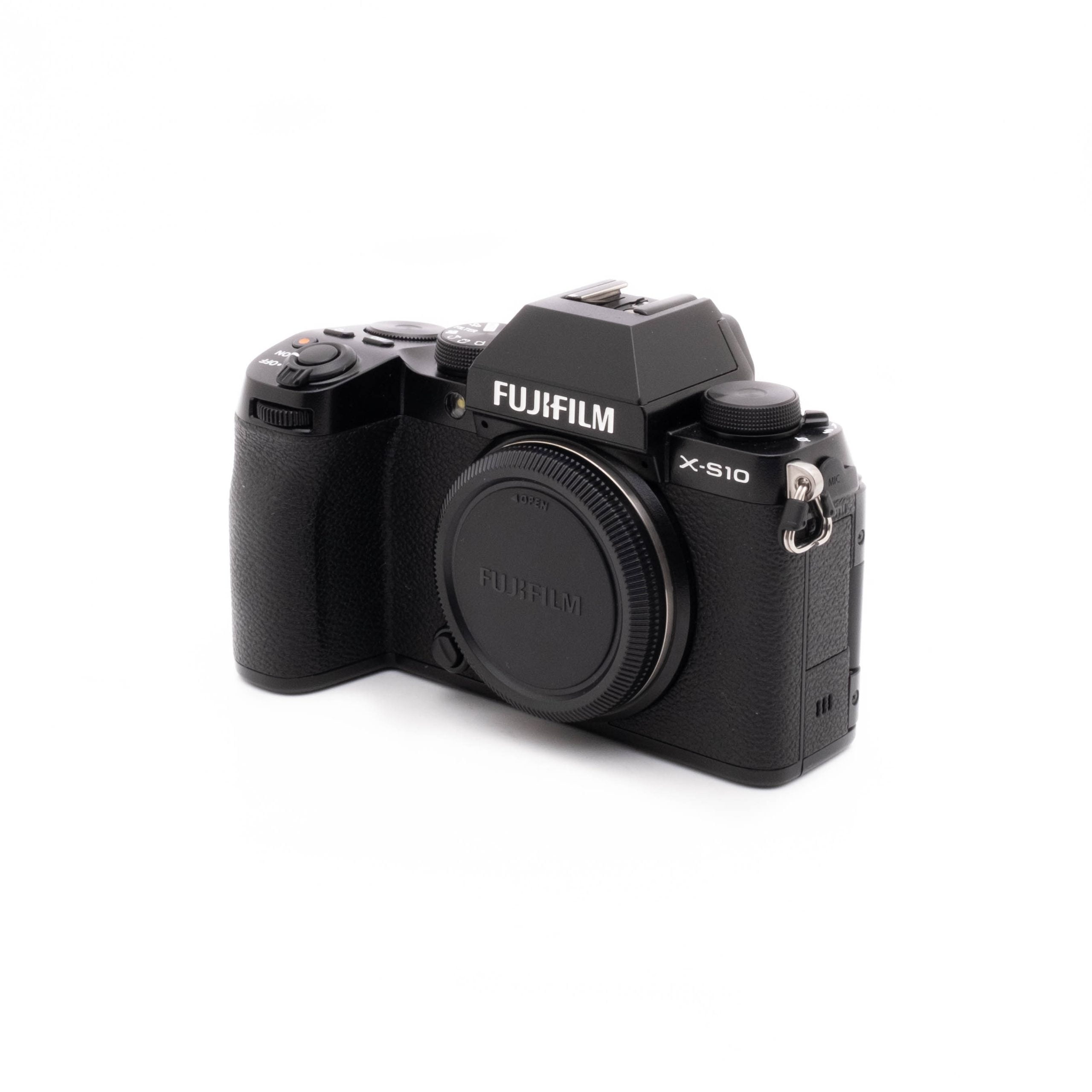 Fujifilm X-S10-1 Fujifilm X-S10 (SC 1189)- Käytetty digitaalikamera näkyy valkoisella taustalla. Mustaan kameraan ei ole kiinnitetty objektiivia, objektiivin kiinnityssuojus on paikallaan ja mallin nimi näkyy selvästi rungossa.