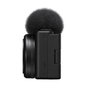 Sivukuva Sony ZV-1F -kompaktikamerasta, kompaktista mustasta digitaalikamerasta, jossa on objektiivi ja sumea tuulisuoja äänen kohinan vähentämiseksi, eristettynä valkoiselta taustalta.