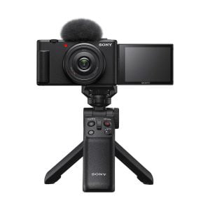 Musta Sony ZV-1F -kompaktikamera, jossa on ulosvedettävä näyttö ja yläosan mikrofoni, asennettuna kompaktin Sonyn jalustakahvan varaan, valkoista taustaa vasten.