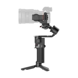 DJI RS 3 Mini -gimbaali, musta käsikäyttöinen kameran gimbal-stabilisaattori, jossa on jalusta, on esitetty pitelemässä puoliksi läpinäkyvää kameraa valkoista taustaa vasten.