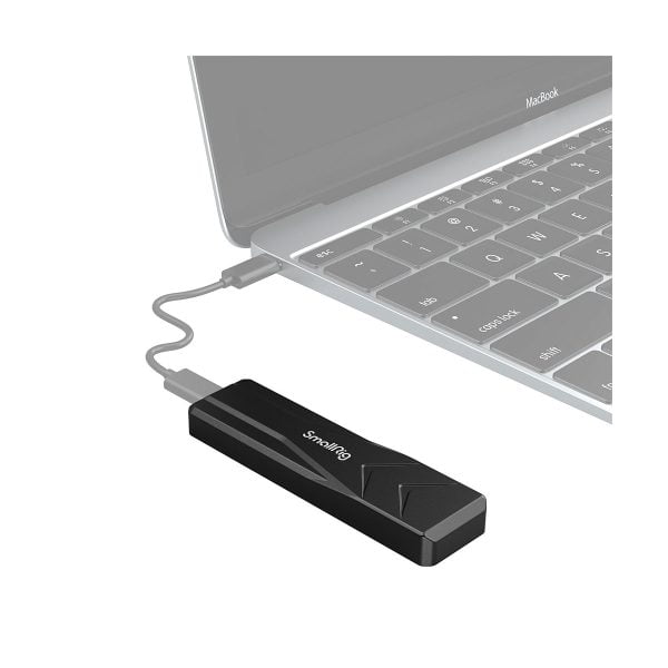 SmallRig 3479 M.2 SSD Enclosure SD-01, musta USB-laite, on liitetty kannettavaan tietokoneeseen lyhyellä USB-kaapelilla, ja kannettavan tietokoneen näppäimistön ja ohjauslevyn osat ovat osittain näkyvissä.