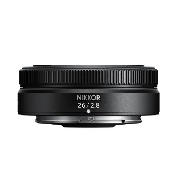 Pienikokoinen musta Nikon Nikkor Z 26mm f/2.8 -objektiivi näkyy valkoista taustaa vasten, ja siinä on kuvioitu tarkennusrengas ja "26/2.8"-merkintä etupuolella.