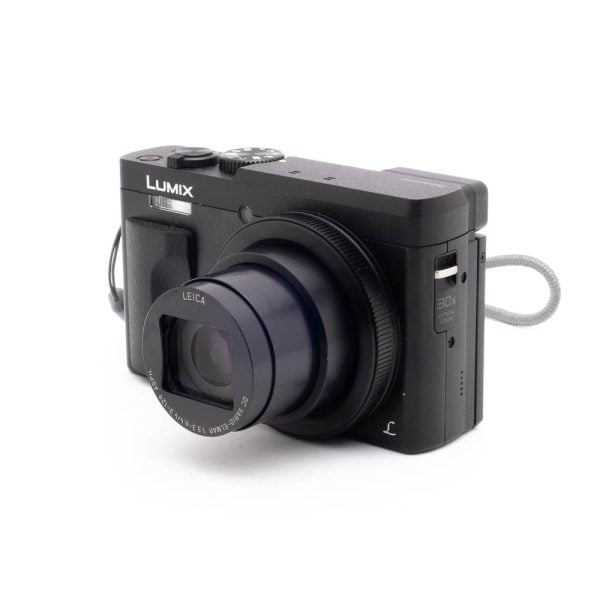 Panasonic DC-TZ90 7657-4 Panasonic Lumix DC-TZ90 - Käytetty digitaalikamera on kuvattu vasemmalle kallistettuna valkoisella taustalla, ja siihen on kiinnitetty osittain laajennettu Leica-zoom-objektiivi ja harmaa rannehihna.