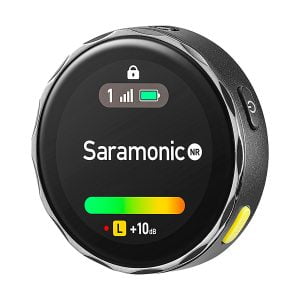 Lähikuva pyöreästä Saramonic BlinkMe B2 -langaton mikrofonijärjestelmä-lähettimestä, jossa on digitaalinen näyttö, jossa näkyy signaalin voimakkuus, akku ja äänenvoimakkuus sekä mustat, hopeiset ja keltaiset painikkeet.
