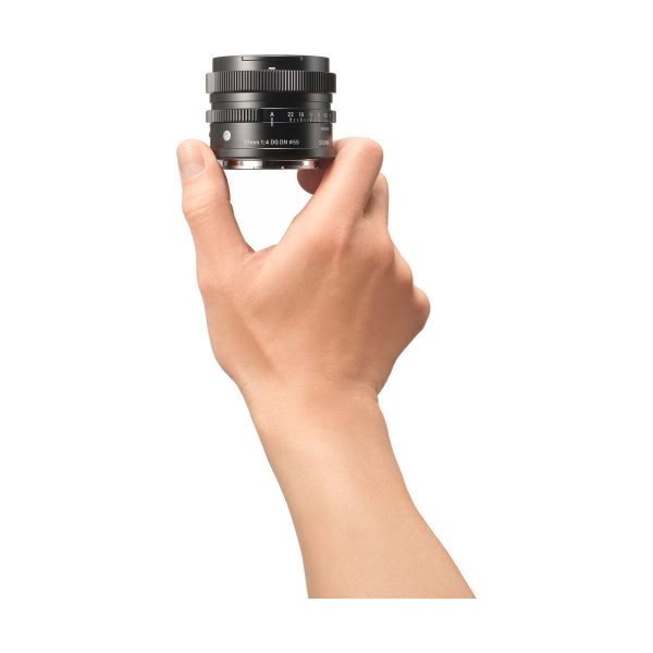 Käsi pitää Sigma 17mm f/4 DG DN DN Contemporary -objektiivia Sonylle pystyssä valkoista taustaa vasten. Mustassa objektiivissa on näkyvät merkinnät ja säätörenkaat, ja käsi näkyy sivulta.