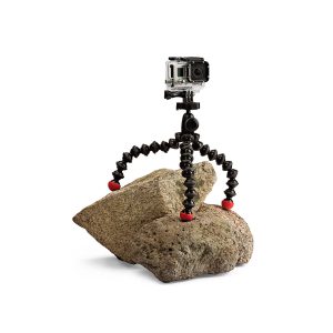 JOBY GorillaPod Action GoPro Jalusta, jossa on punaiset jalat, pitää GoPro-kameraa kahdella epätasaisella kivellä valkoista taustaa vasten.