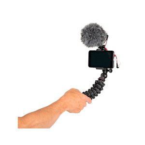 Käsi pitää JOBY GripTight PRO 2 GorillaPod Jalustakit Puhelimelle kiinnitetyn älypuhelimen, ulkoisen mikrofonin, jossa on karvainen tuulisuoja, ja kaapelit, jotka muodostavat kannettavan vloggausasetelman.